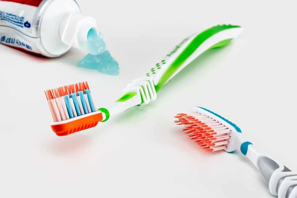 Two toothbrushes lie next to an open toothpaste.
