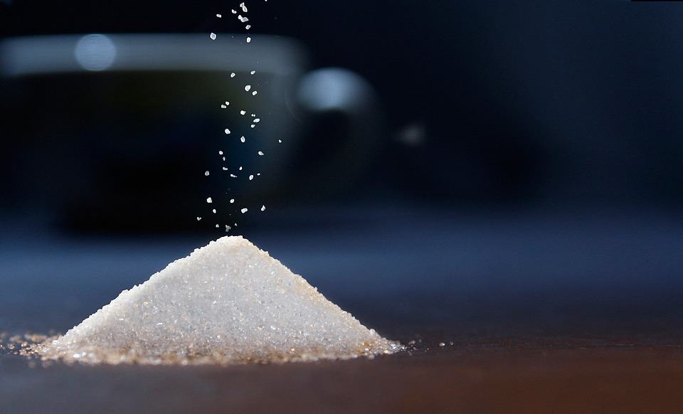A pile of sugar is being slowly sprinkled onto a kitchen counter.